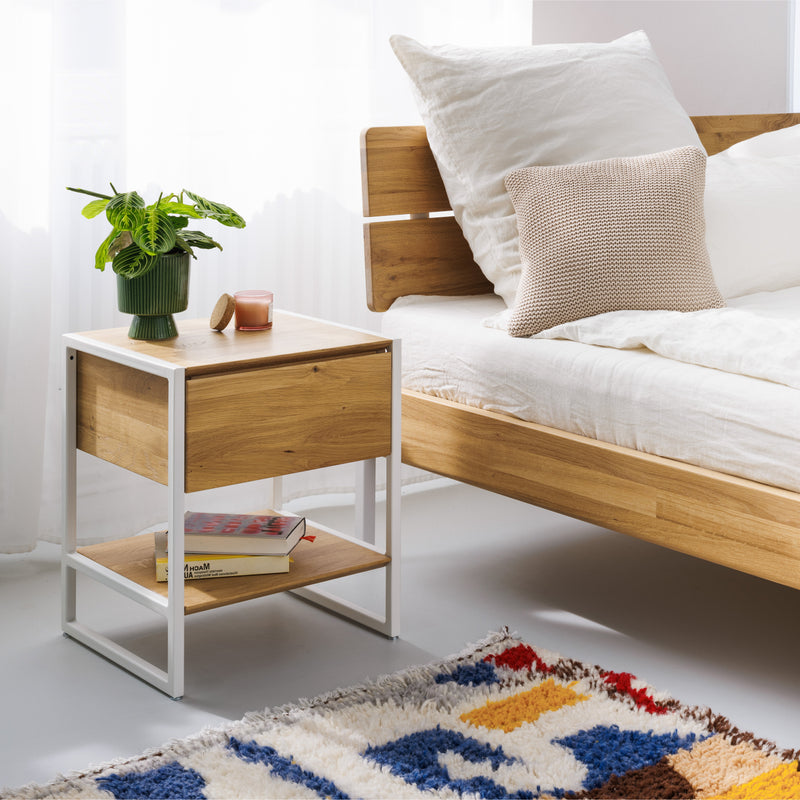 Schlichter Nachttisch mit Schublade neben minimalistischen Bett aus massiver Eiche mit Metallakzenten und nachhaltiger Bettwäsche